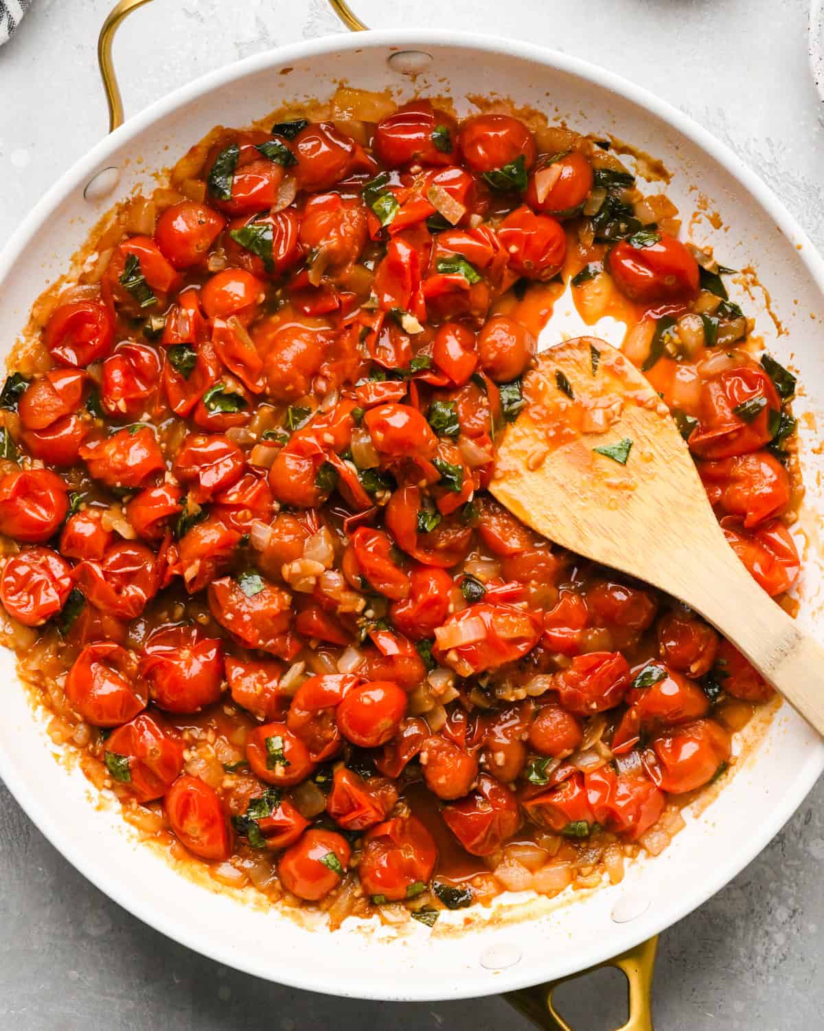 Making pasta with burrata cheese: close-up photo of sautéed tomatoes, garlic, basil, and onions being stirred with a wooden spoon in a large skillet.