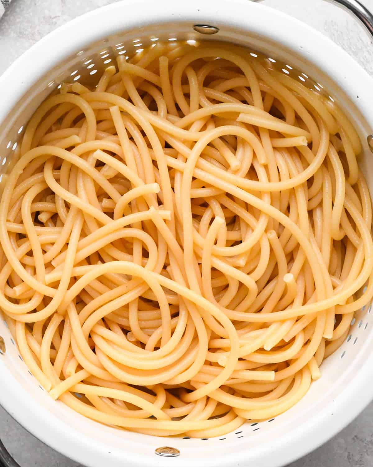 Making pasta with burrata cheese: overhead photo of cooked pasta noodles shown in a white colander after draining the water.