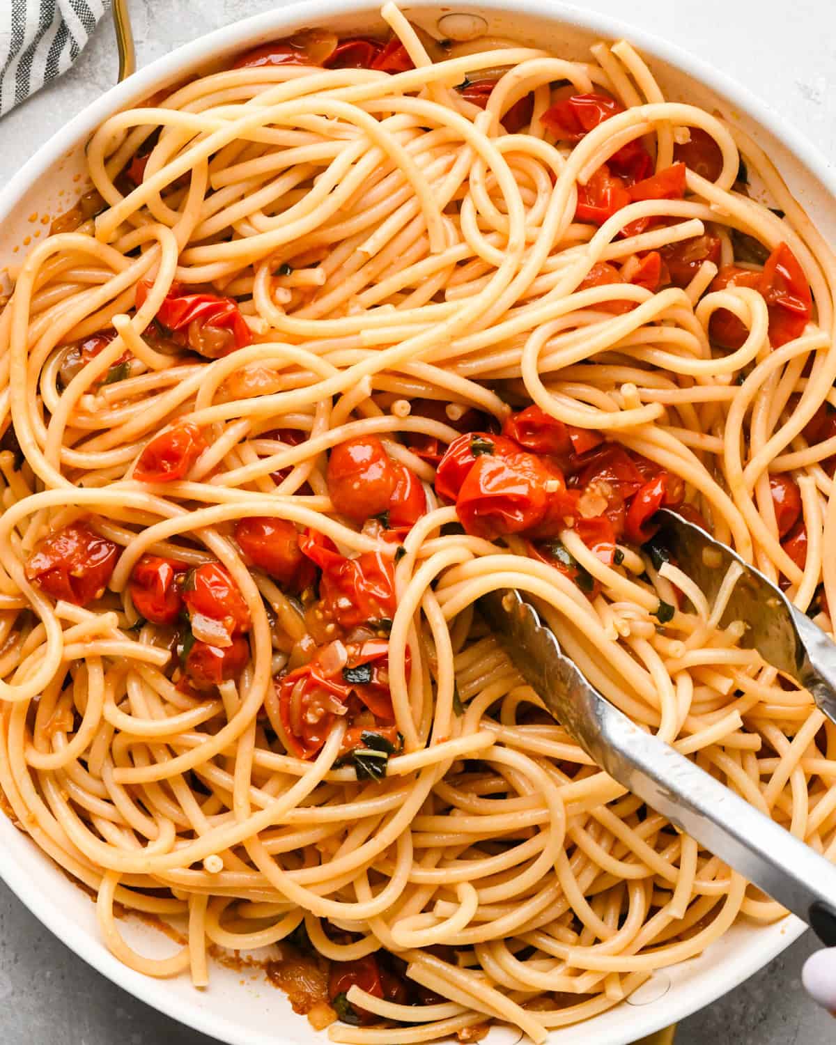Making pasta with burrata cheese: overhead photo of cooked pasta added to the sautéed vegetables in a skillet and being tossed together with tongs.