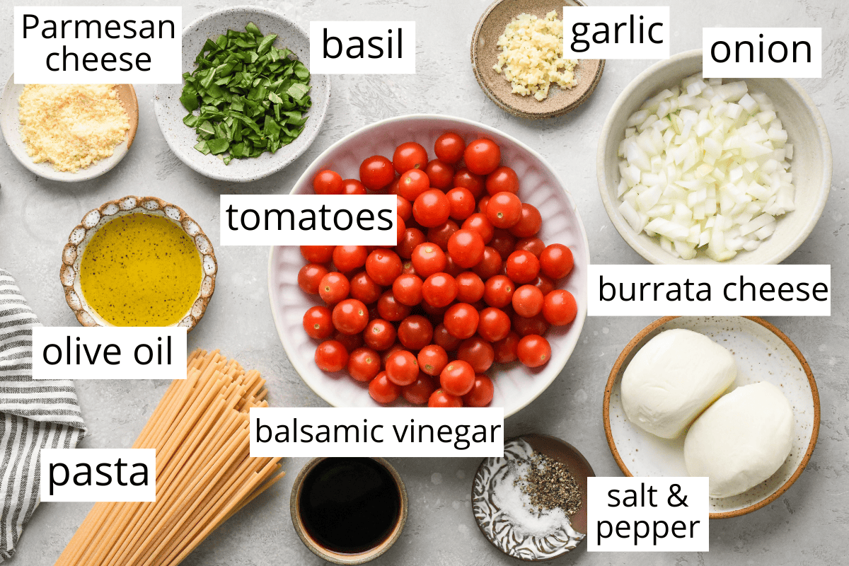 Overhead photo of the labeled ingredients for pasta with burrata cheese, including pasta, olive oil, parmesan cheese, tomatoes, basil, balsamic vinegar, salt and pepper, burrata cheese, onion, and garlic.