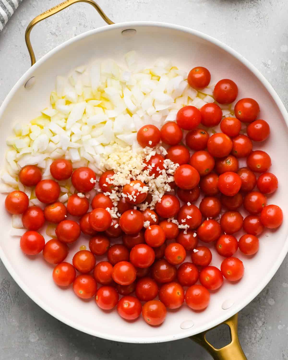 Making pasta with burrata cheese: overhead photo of tomatoes, garlic, and onions shown uncovered in a large gold and white skillet.