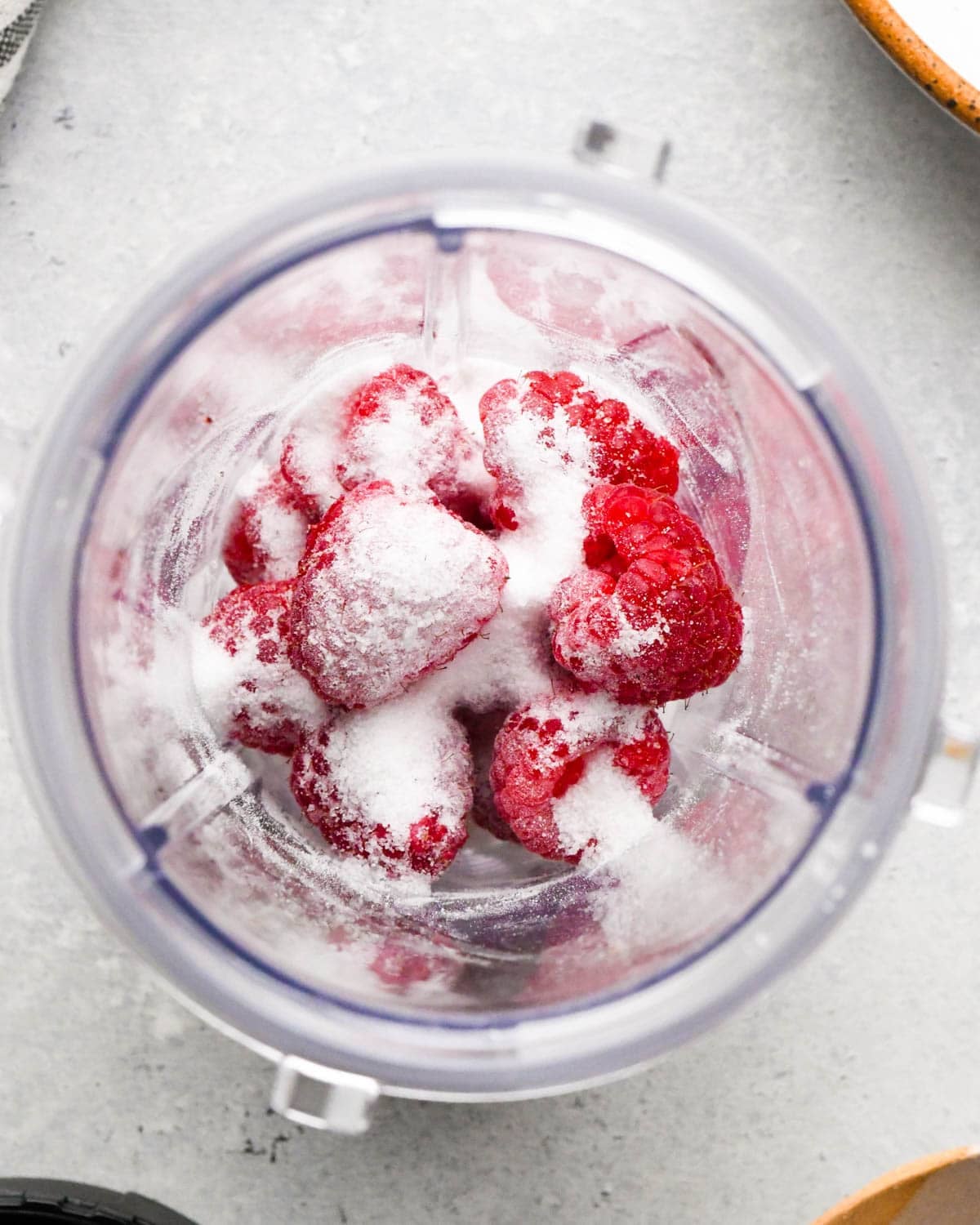 how to make raspberry frosting - overhead view of raspberries and sugar in a small blending container before blending