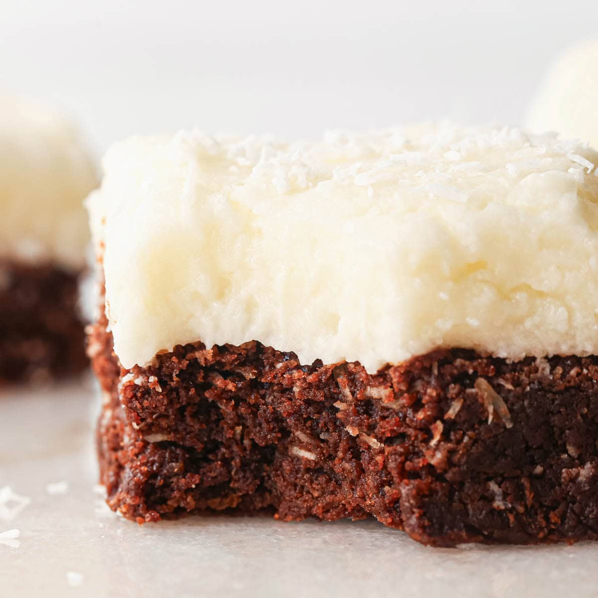 close up photo of a chocolate coconut brownie with coconut frosting, with a bite taken out of it so the fudgy texture and bits of coconut are visible. 