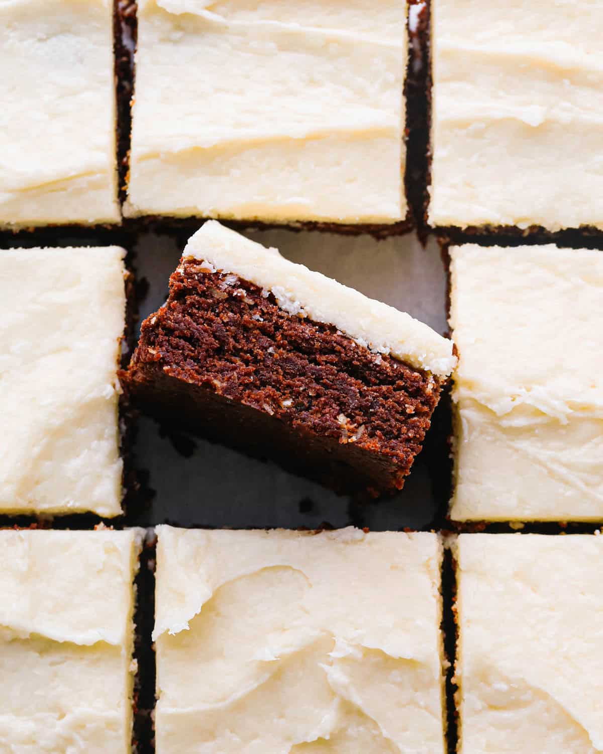 chocolate coconut brownies with coconut frosting cut into 9 squares, the middle is laying on it's side so the fudgy texture is visible