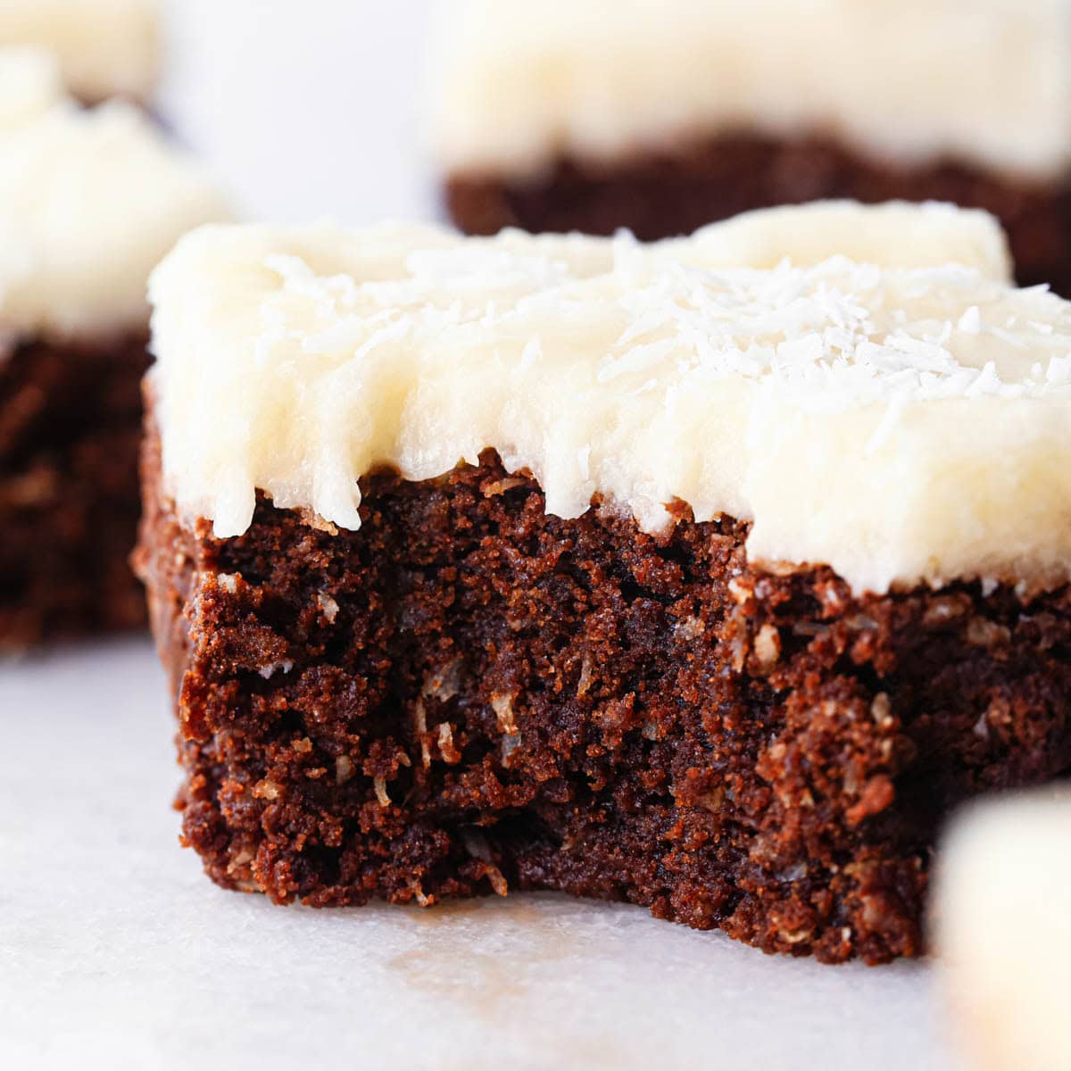 up close photo of a chocolate coconut brownie with coconut frosting with a bite taken out of 