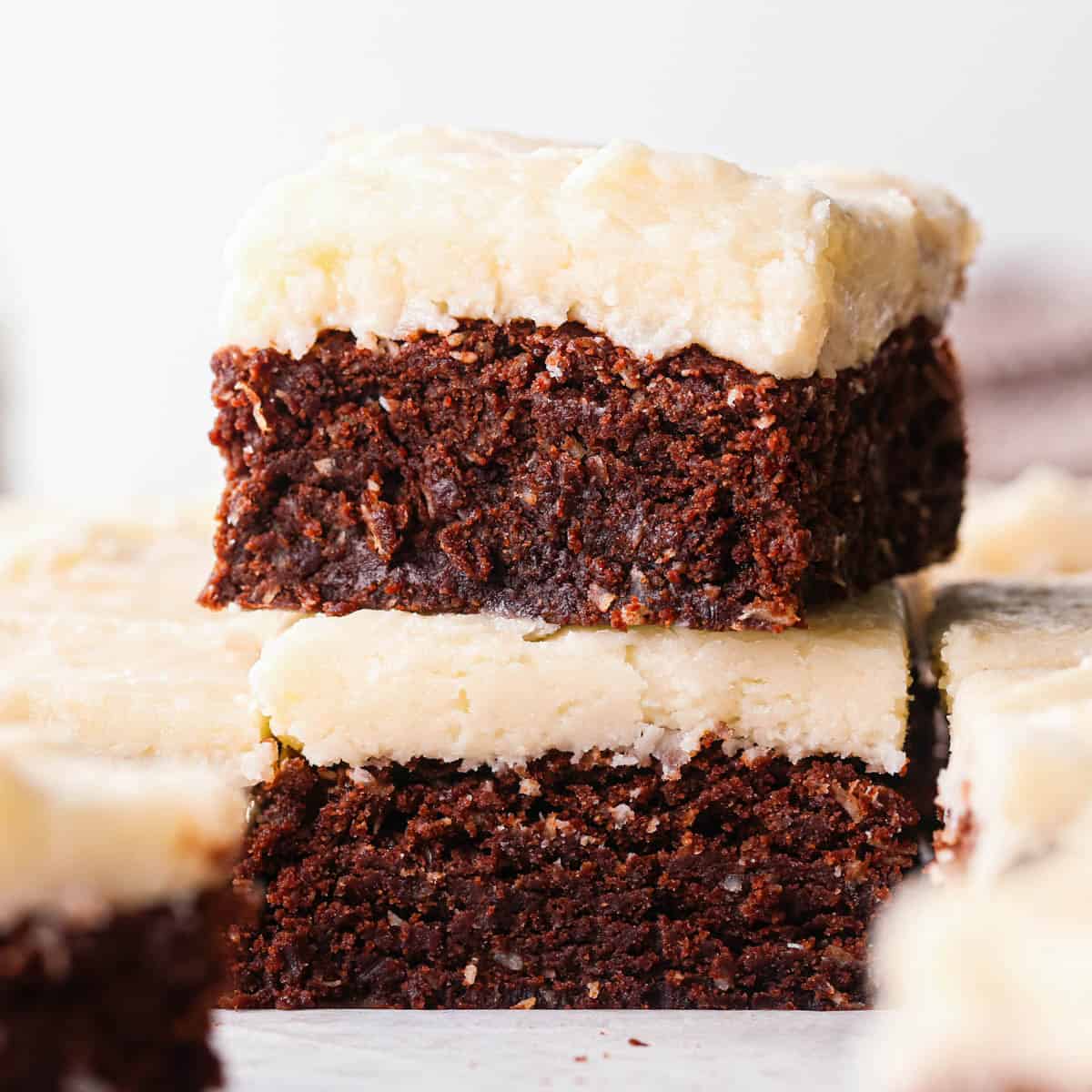 a stack of two chocolate coconut brownies with coconut frosting, surrounded by other coconut brownies