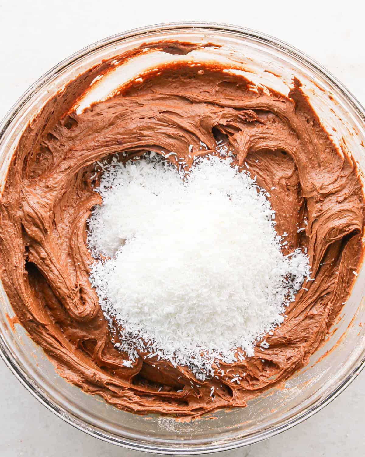making coconut brownies - shredded coconut added to the brownie batter in a glass bowl before mixing