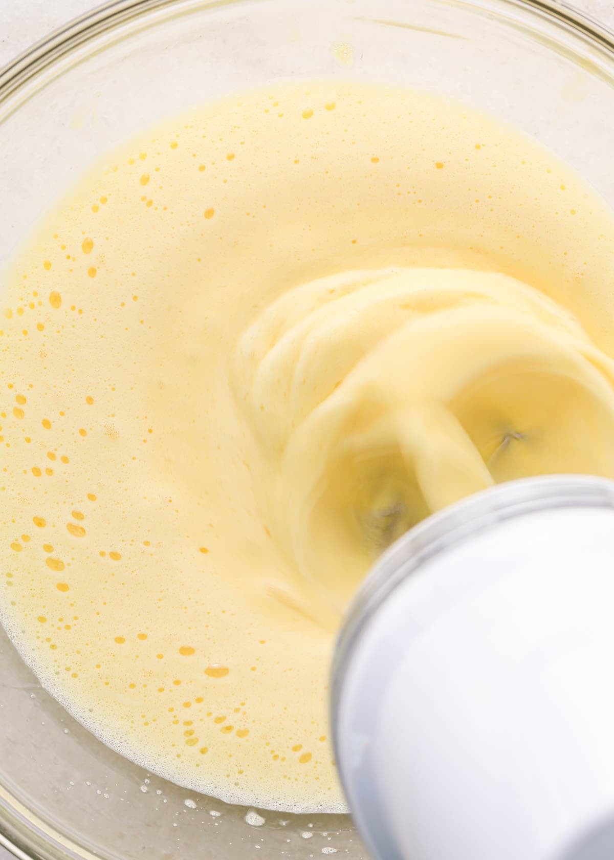 making coconut brownies - eggs being beaten with a white hand mixer in a glass bowl