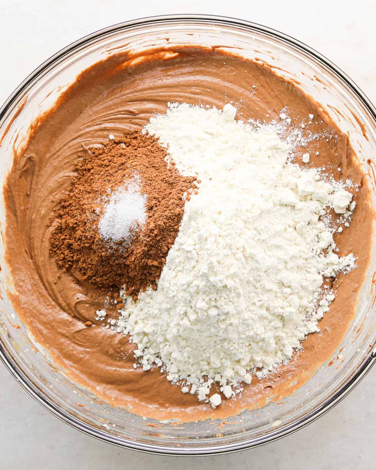 making coconut brownies - flour, cocoa powder and salt added to the wet ingredients in a glass bowl before mixing