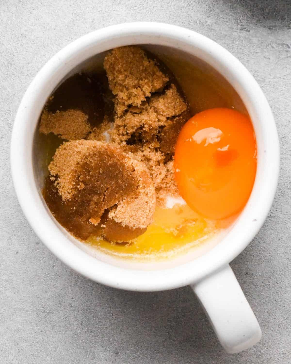 making a mug cookie - sugar, brown sugar, egg yolk and vanilla added to the melted butter in a white mug before mixing