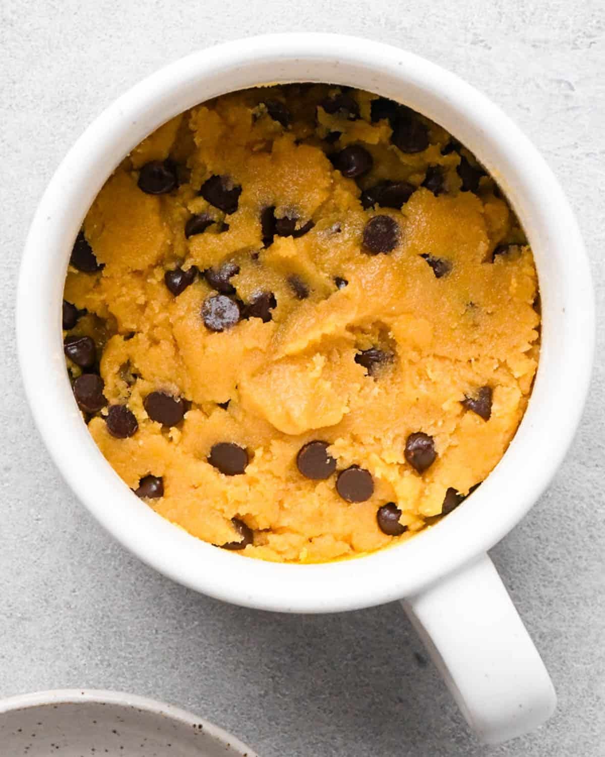 making a cookie in a mug - dough with chocolate chips mixed in in a white mug