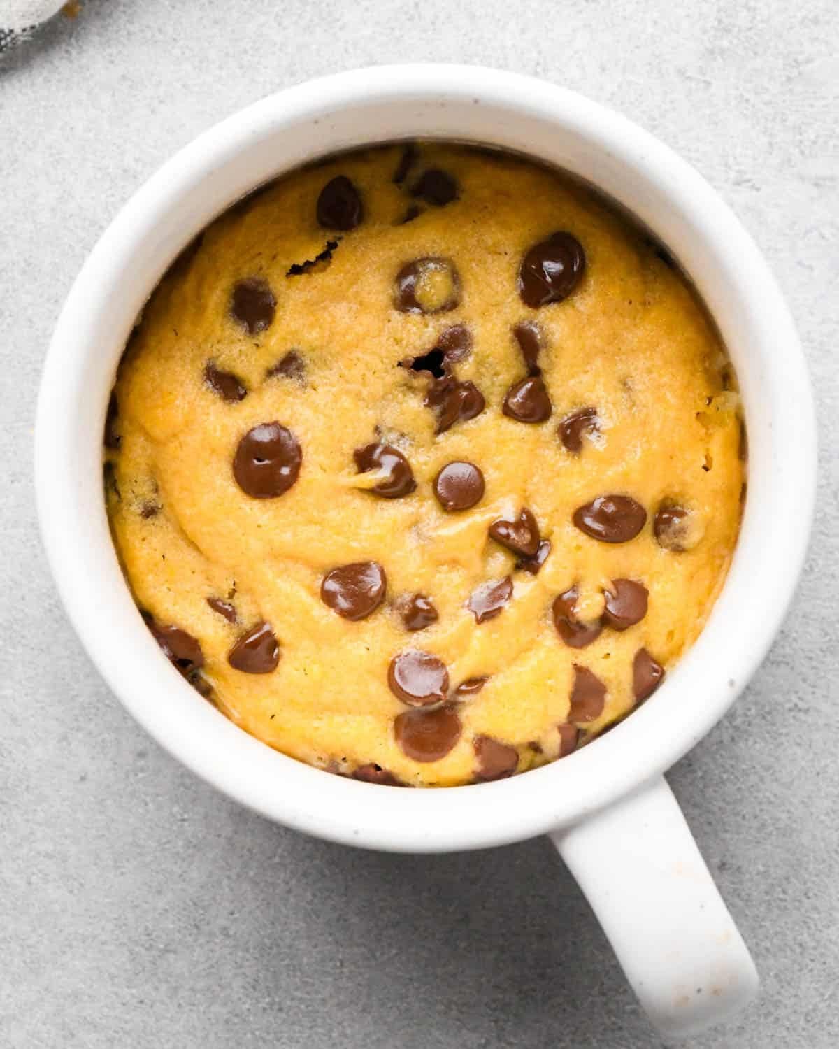 overhead photo of a chocolate chip cookie in a mug with melty chocolate chips on top. 