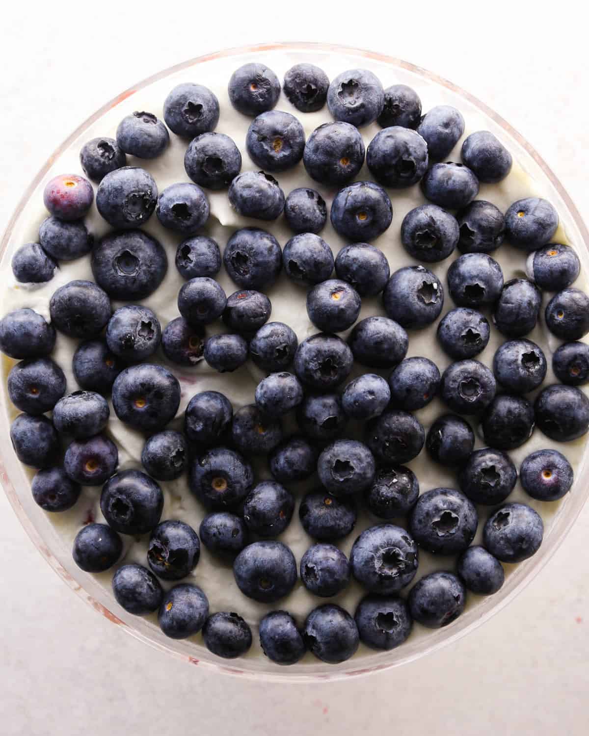 how to make a trifle with berries - blueberries put on top of the whipped cream in a glass trifle dish.