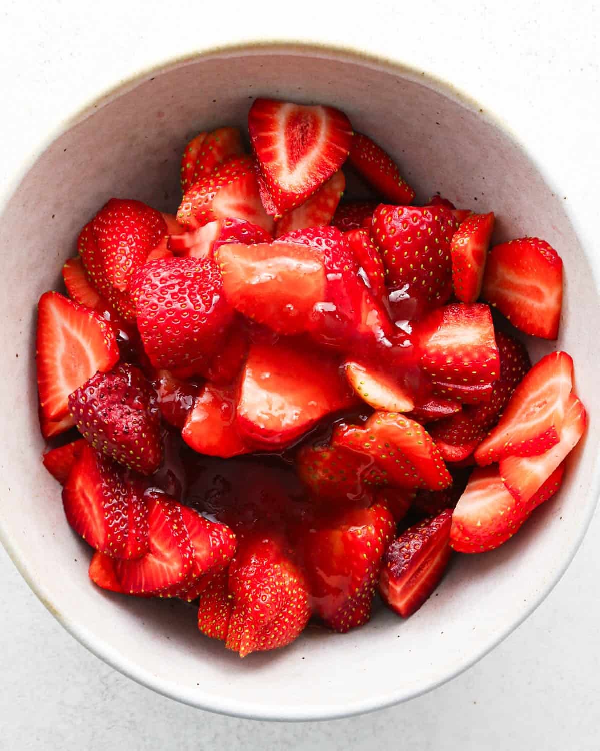 how to make a trifle with berries - the jam sauce poured over the strawberries in a white bowl before mixing