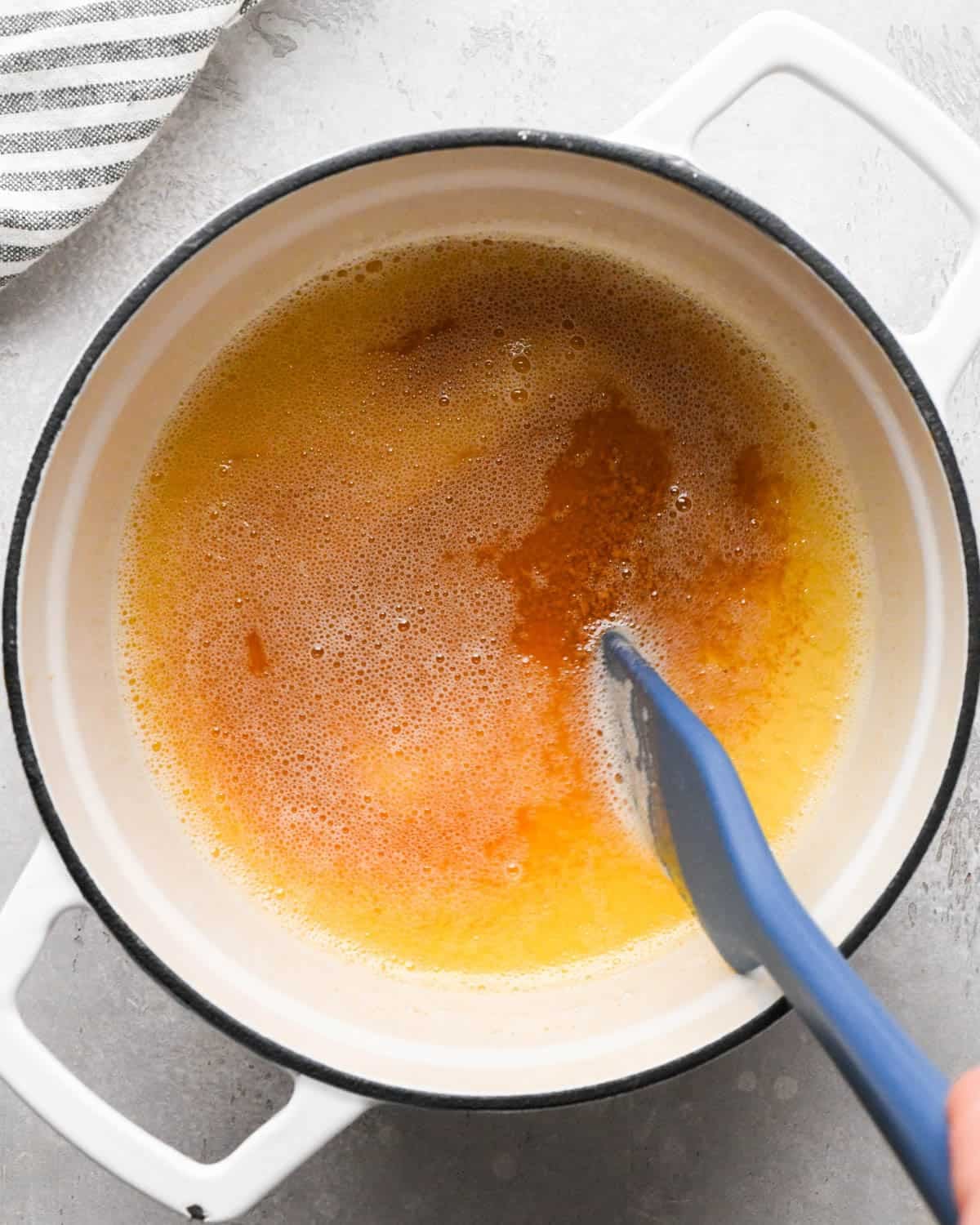 browning butter for brown butter brownies - foamy, dark amber browned butter in a pot with a blue spatula