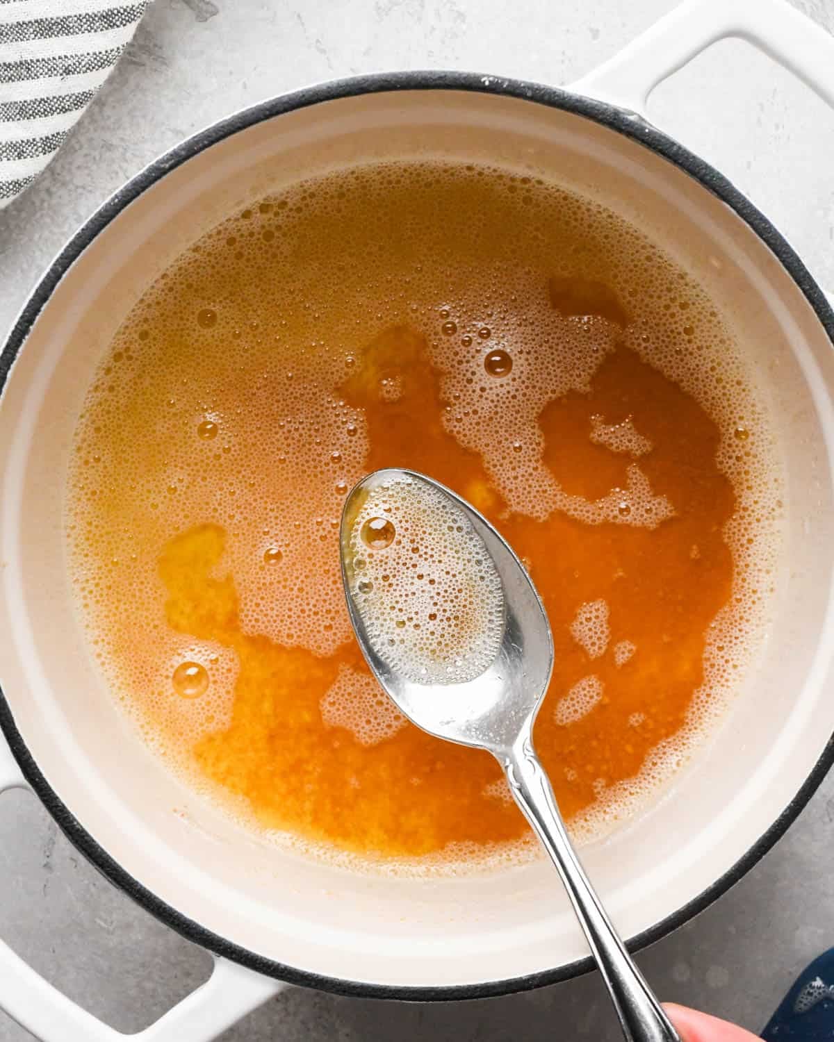 browning butter for brown butter brownies - a silver spoon holding a scoop of dark amber browned butter in a pot