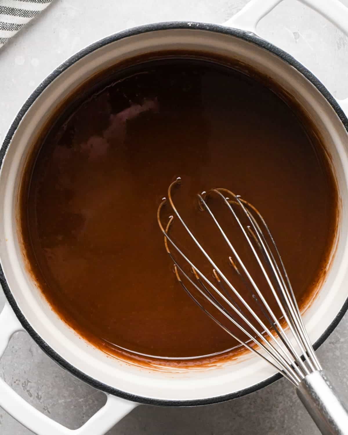 making brown butter brownies - chocolate chips and browned butter melted in a white pot with a black rim and a metal whisk in the pot
