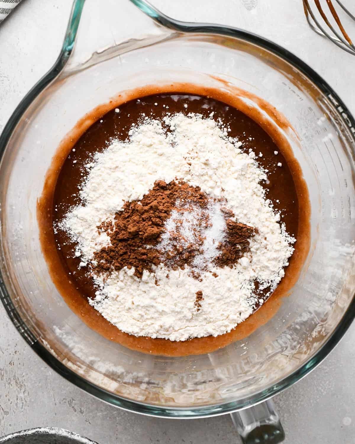 making brown butter brownies - flour, cocoa powder and salt added to the wet ingredients in a glass mixing bowl before mixing