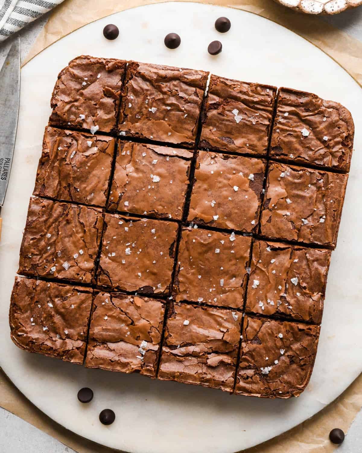 brown butter brownies cut into 16 squares on a round marble serving plate topped with flaky sea salt