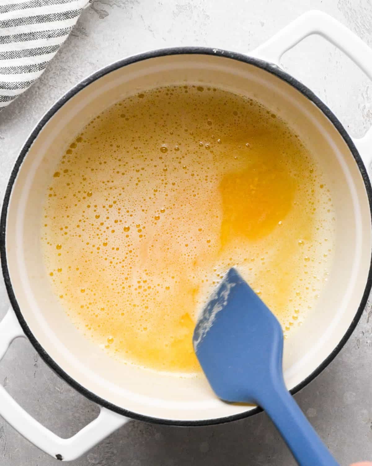 browning butter for brown butter brownies - melted, foamy and slightly browned butter in a pot with a blue spatula