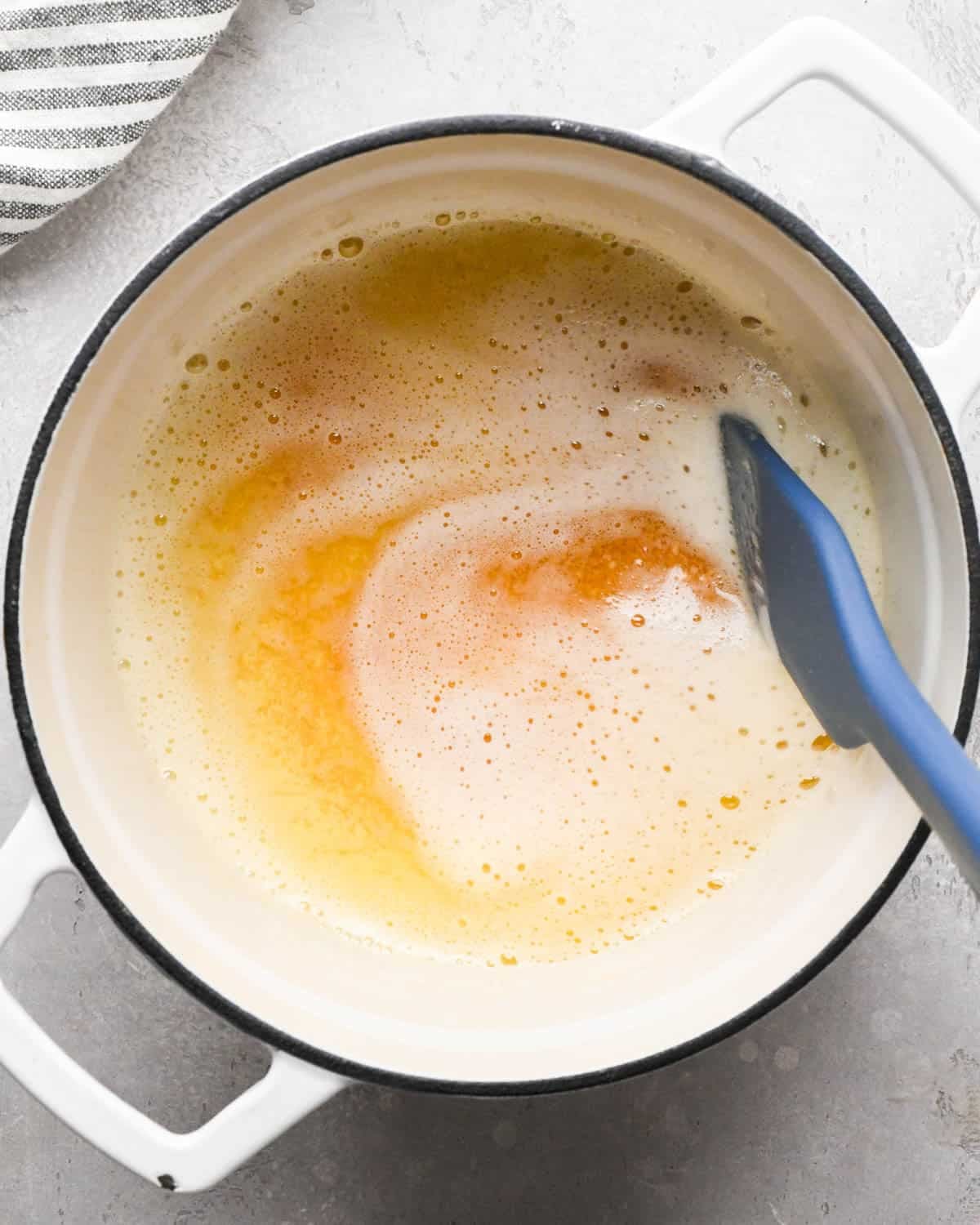 browning butter for brown butter brownies - foamy, amber butter in a pot with a blue spatula