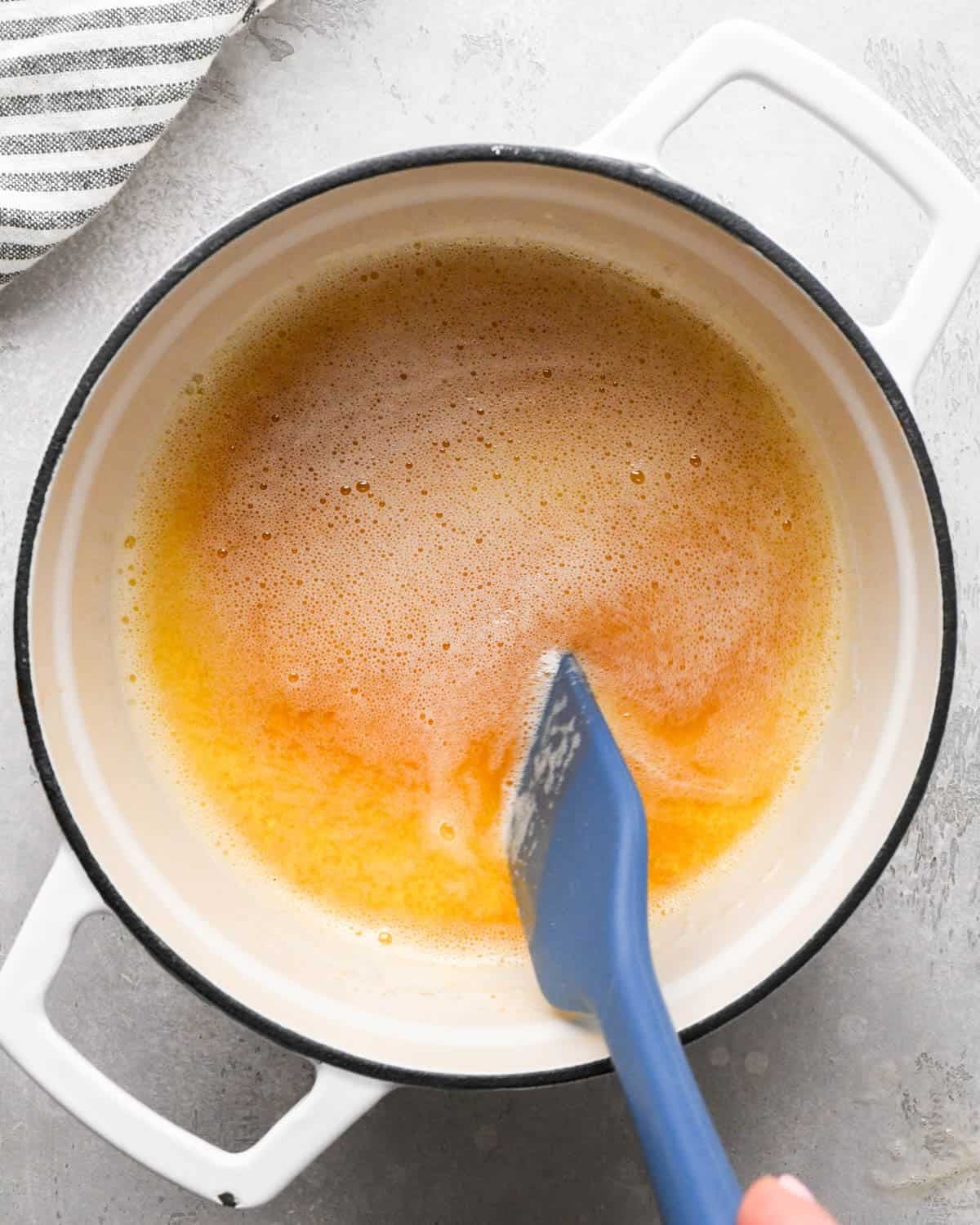 browning butter for brown butter brownies - foamy, amber butter in a pot with a blue spatula