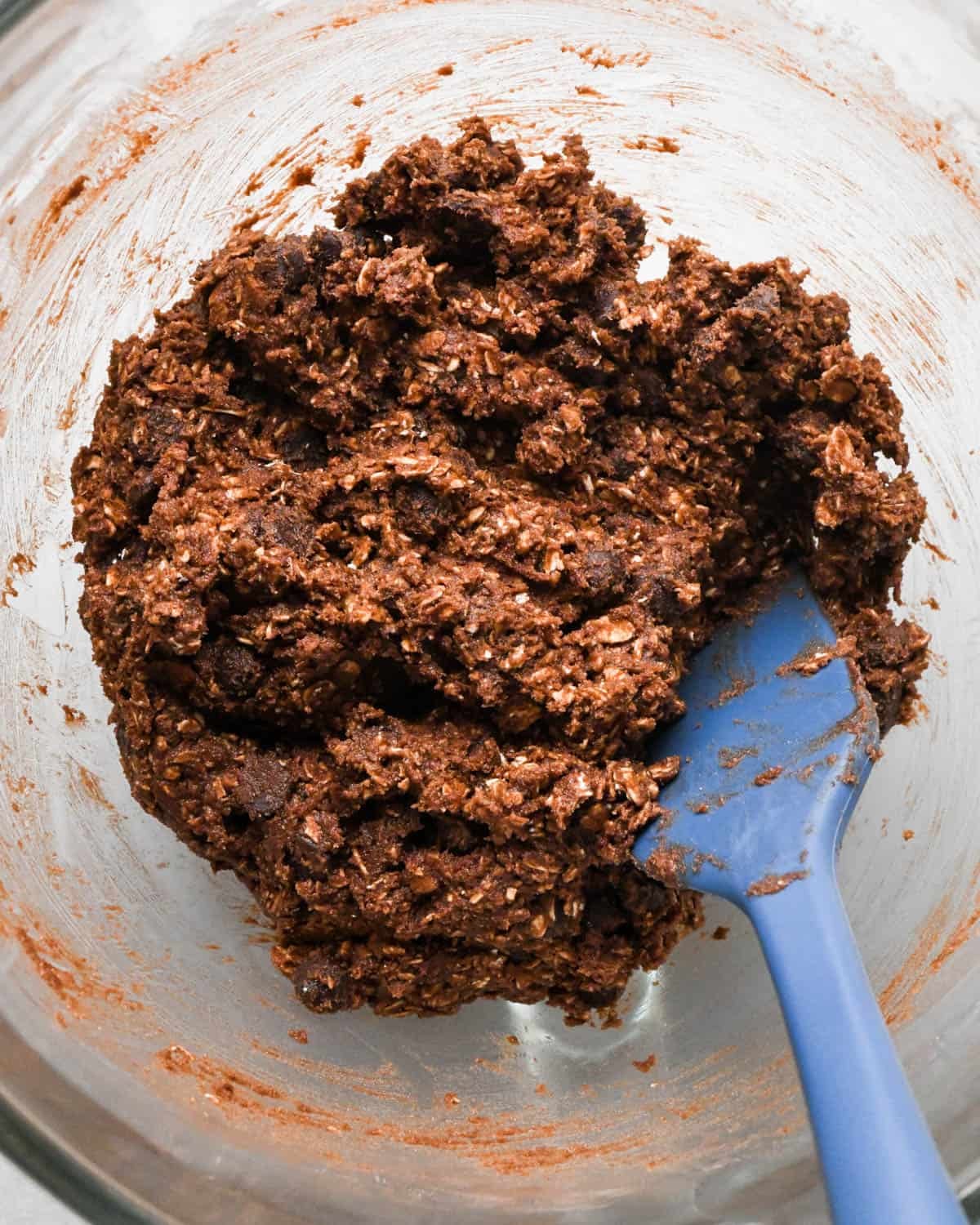 final double chocolate oatmeal cookies dough in a glass bowl with a blue spatula