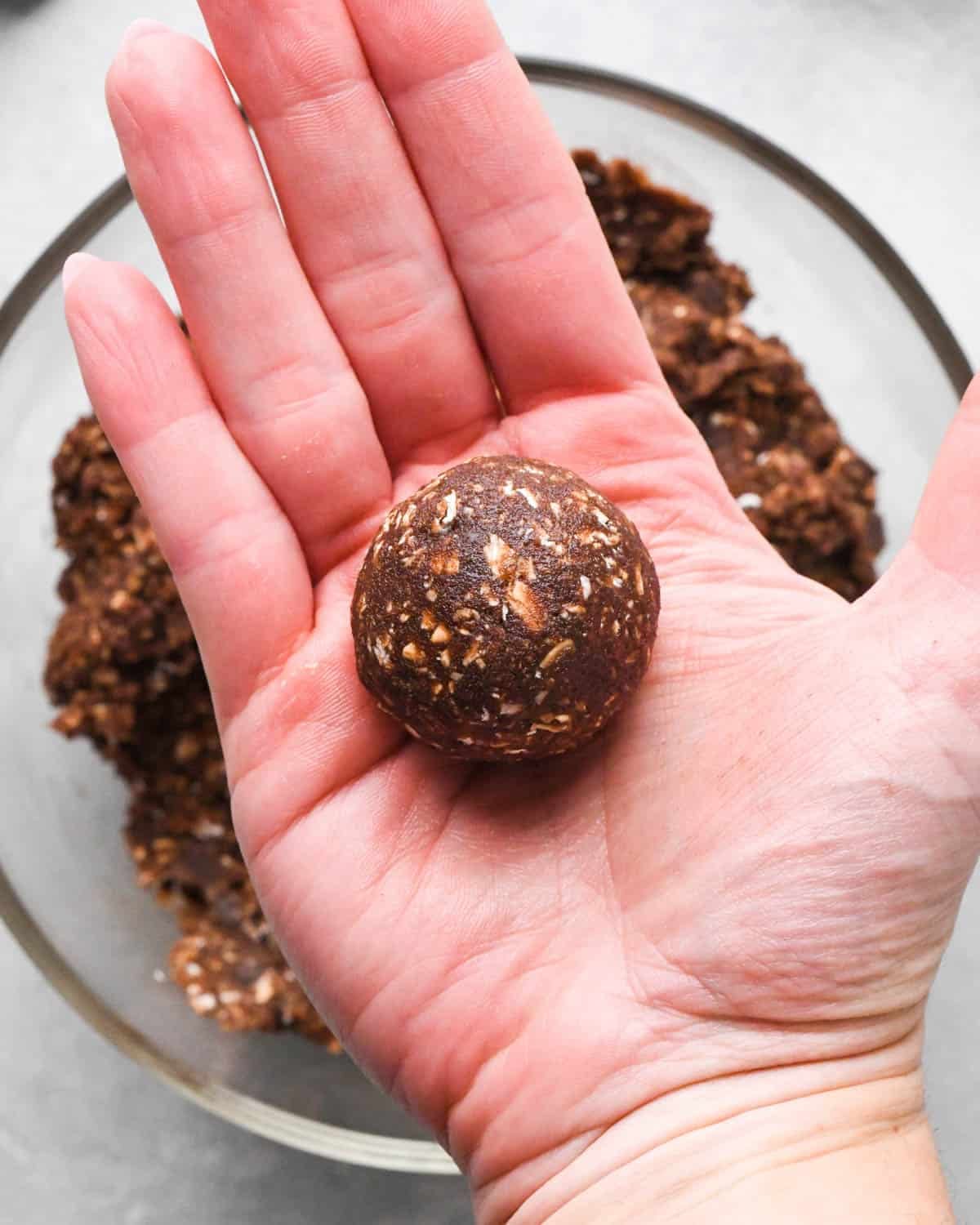 a rolled ball of double chocolate oatmeal cookie dough in a hand hovering over a bowl of cookie dough