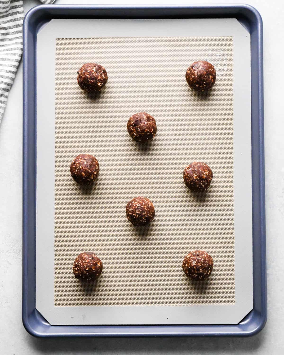 8 double chocolate oatmeal cookie dough balls on a baking sheet lined with a silicone baking mat before baking