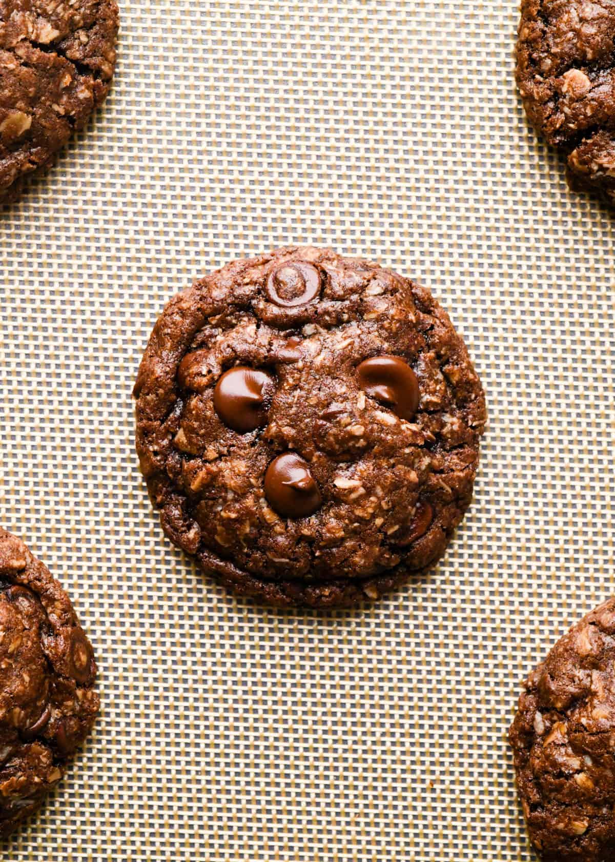 5 double chocolate oatmeal cookies on a baking sheet lined with a silicone baking mat after baking