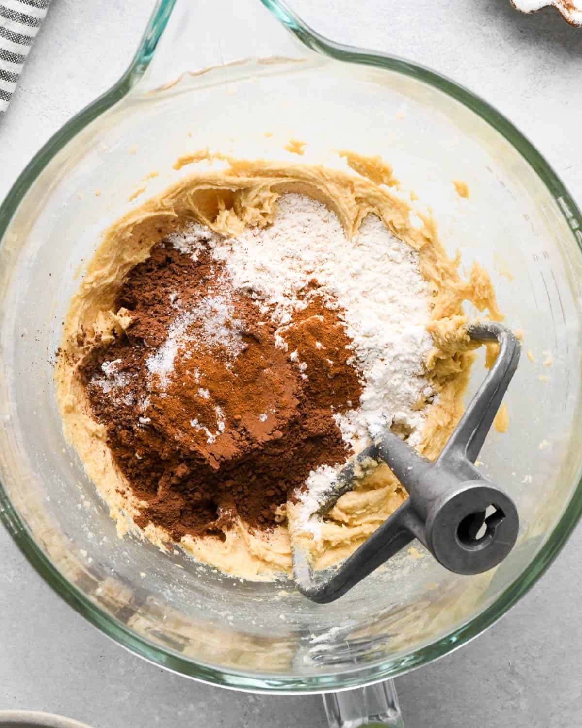 How to Make Chocolate Oatmeal Cookies - flour, cocoa powder, baking soda, baking powder and salt added to the creamed wet ingredients in a glass mixing bowl with a paddle attachment