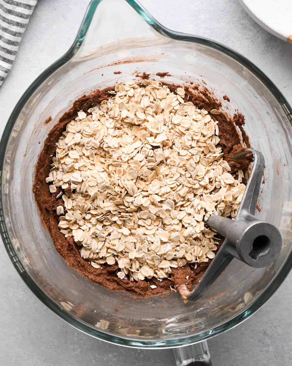 How to Make Chocolate Oatmeal Cookies - oats added to the dough in a glass mixing bowl with the paddle attachment before mixing