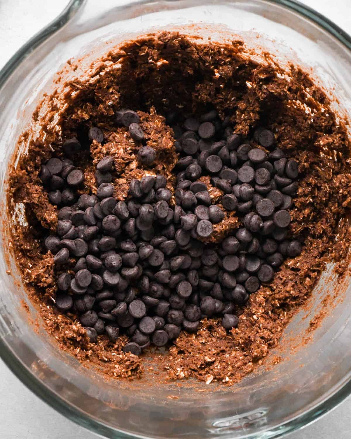 How to Make Chocolate Oatmeal Cookies - chocolate chips added to the dough in a glass mixing bowl before mixing