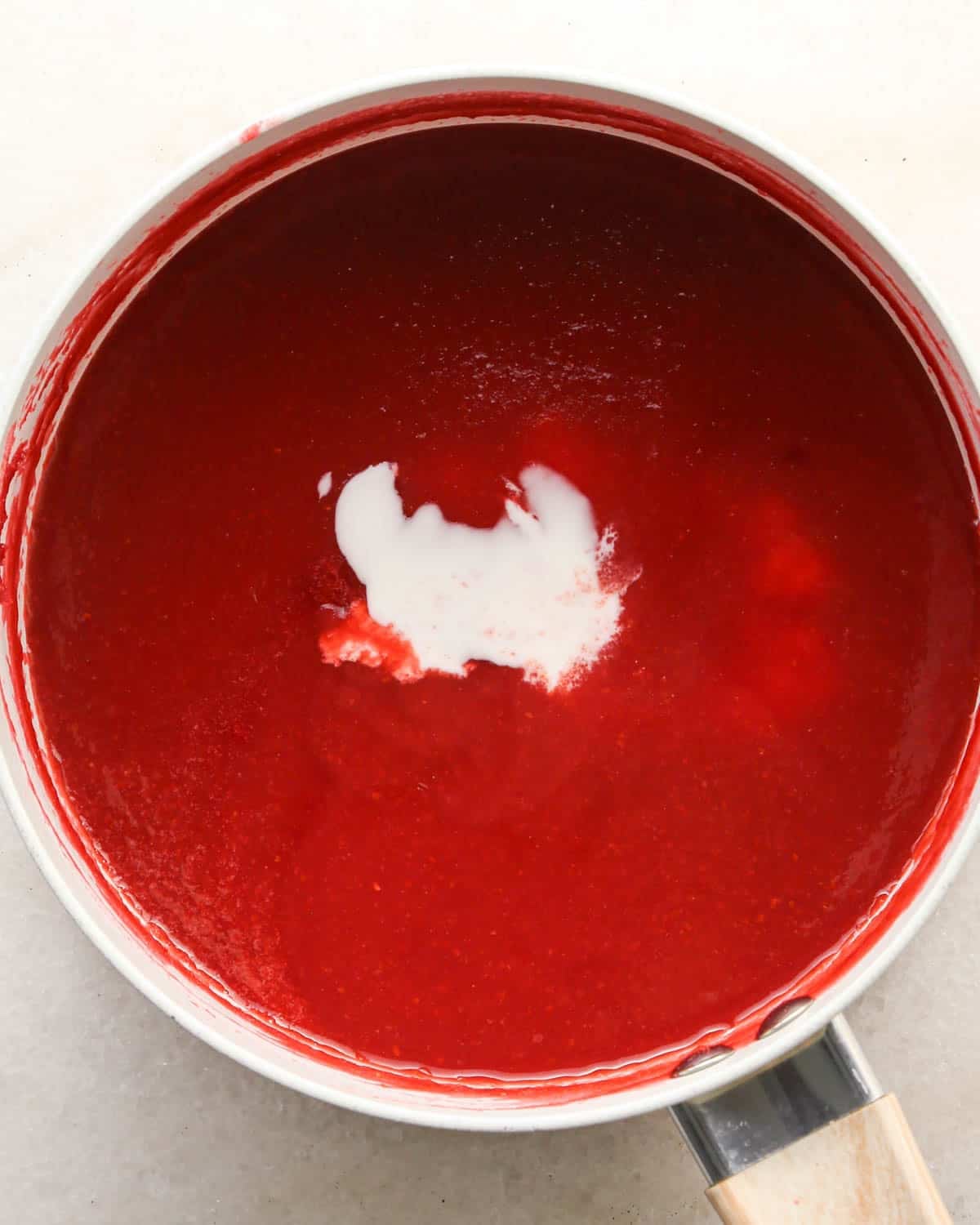 making raspberry filling for a chocolate raspberry cake - cornstarch and water mixture added to the raspberry mixture in a white saucepan before mixing