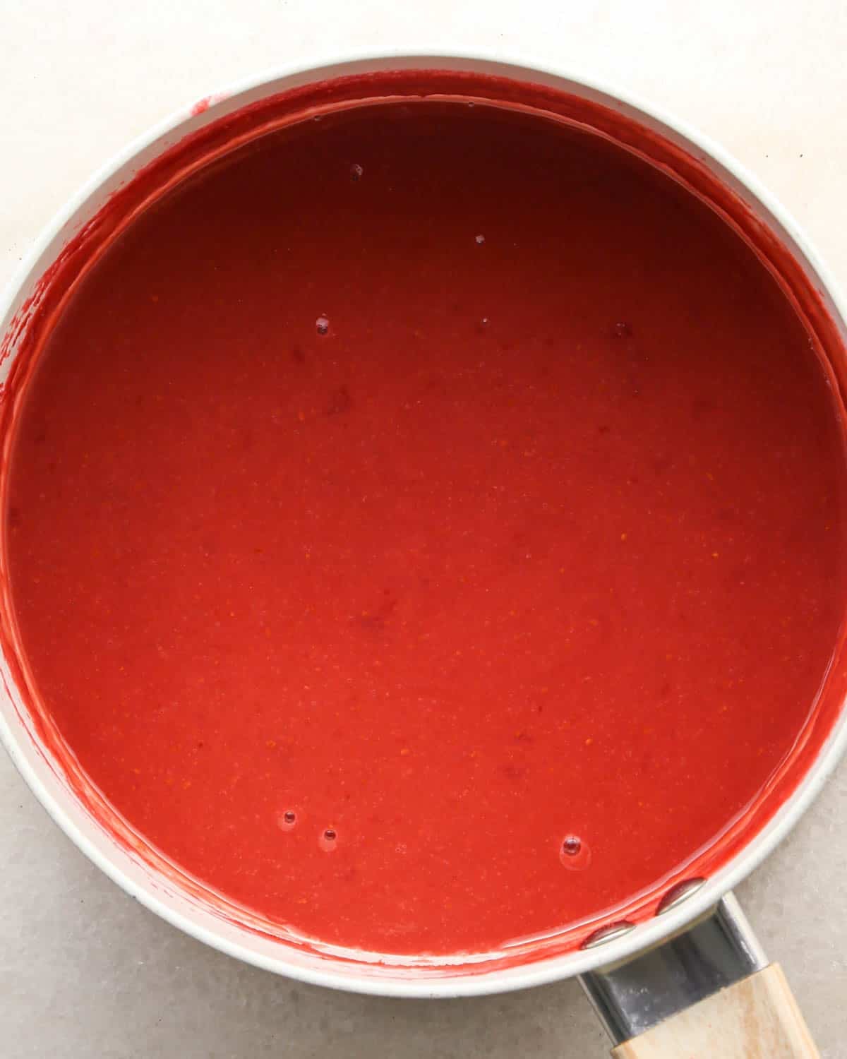 making raspberry filling for a chocolate raspberry cake - cornstarch and water mixture added to the raspberry mixture in a white saucepan after mixing