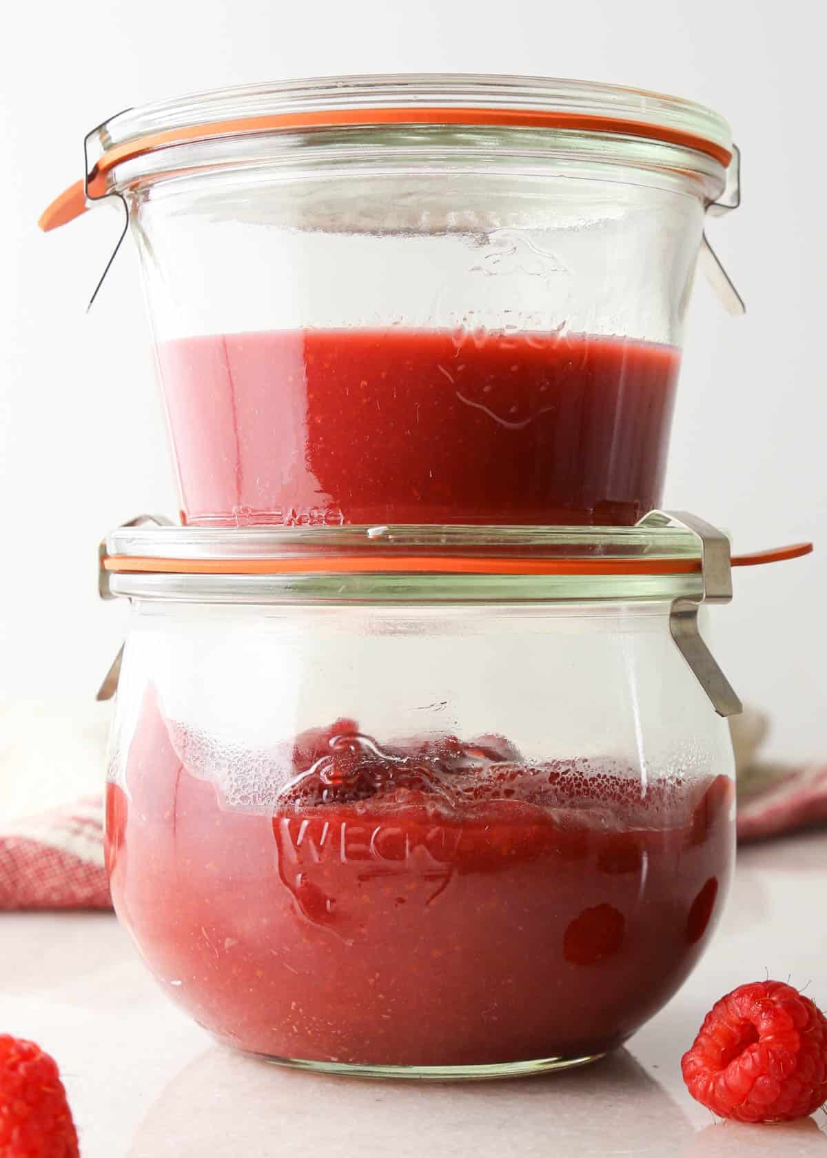 front view of a stack of two glass jars, the top one has the raspberry puree for the frosting, and the bottom one has the thickened raspberry filling