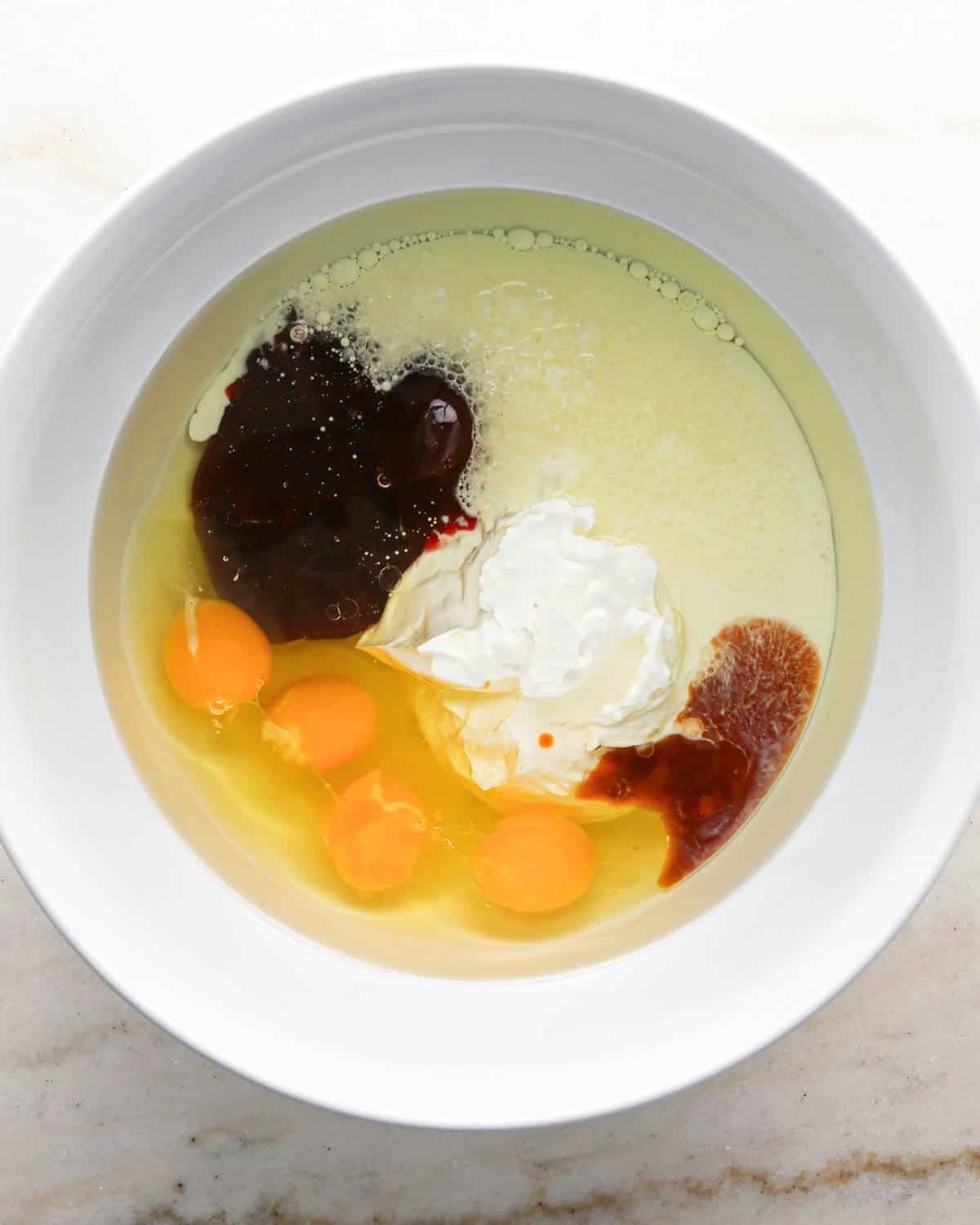 making chocolate raspberry cake - eggs, sour cream, raspberry jam, vanilla, and canola oil in a glass bowl before mixing
