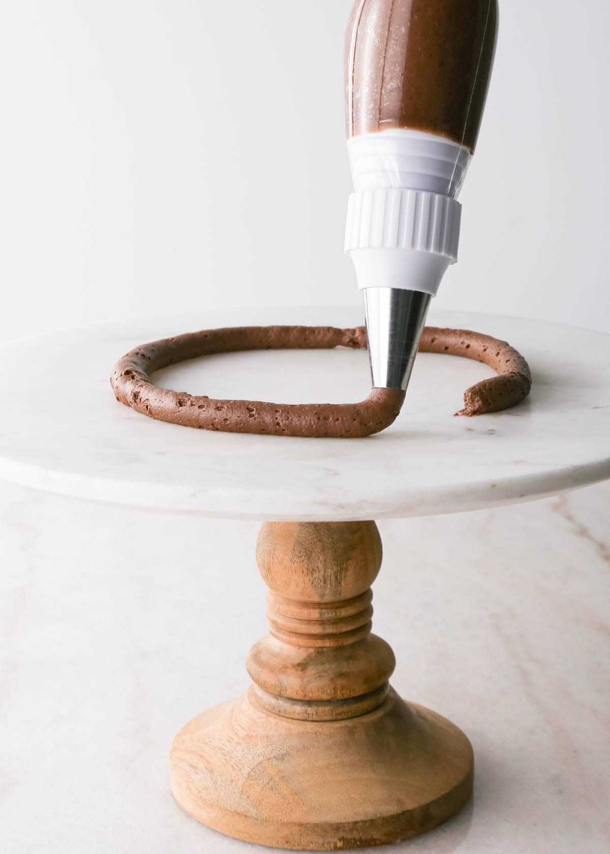 assembling chocolate raspberry cake - piping a circle of chocolate frosting on the cake plate