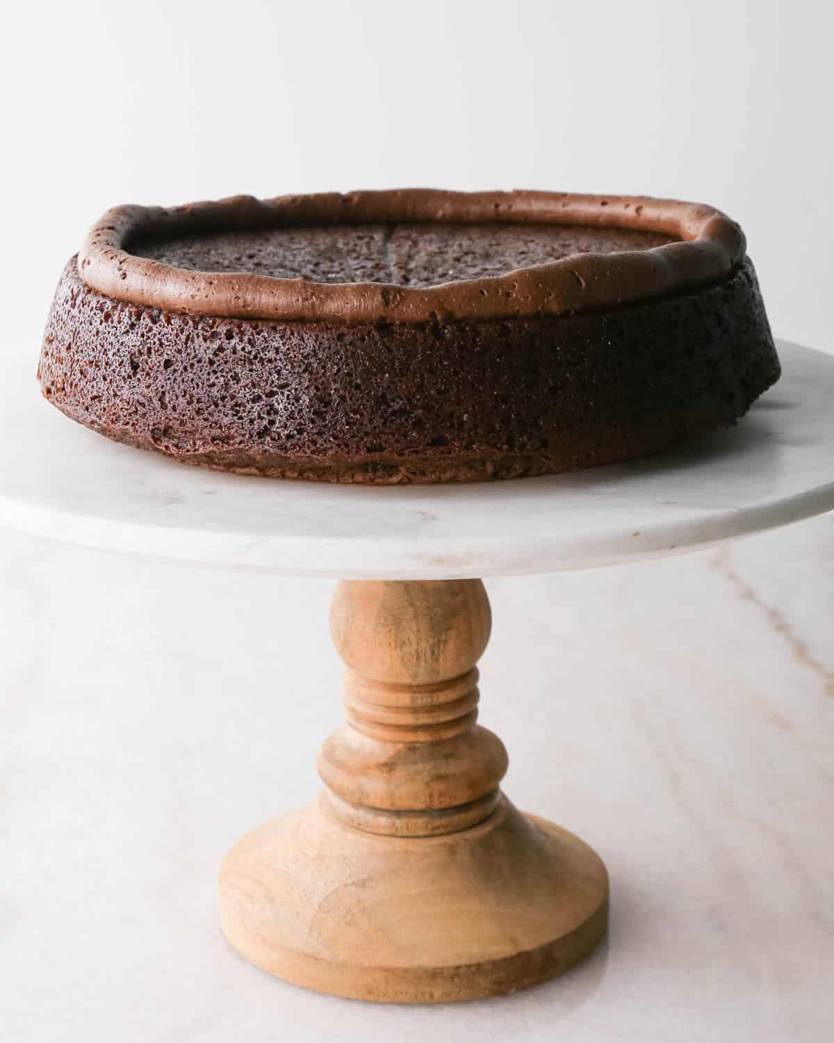 assembling chocolate raspberry cake - a ring of chocolate frosting on the first layer of cake on a white marble cake stand with a wood base