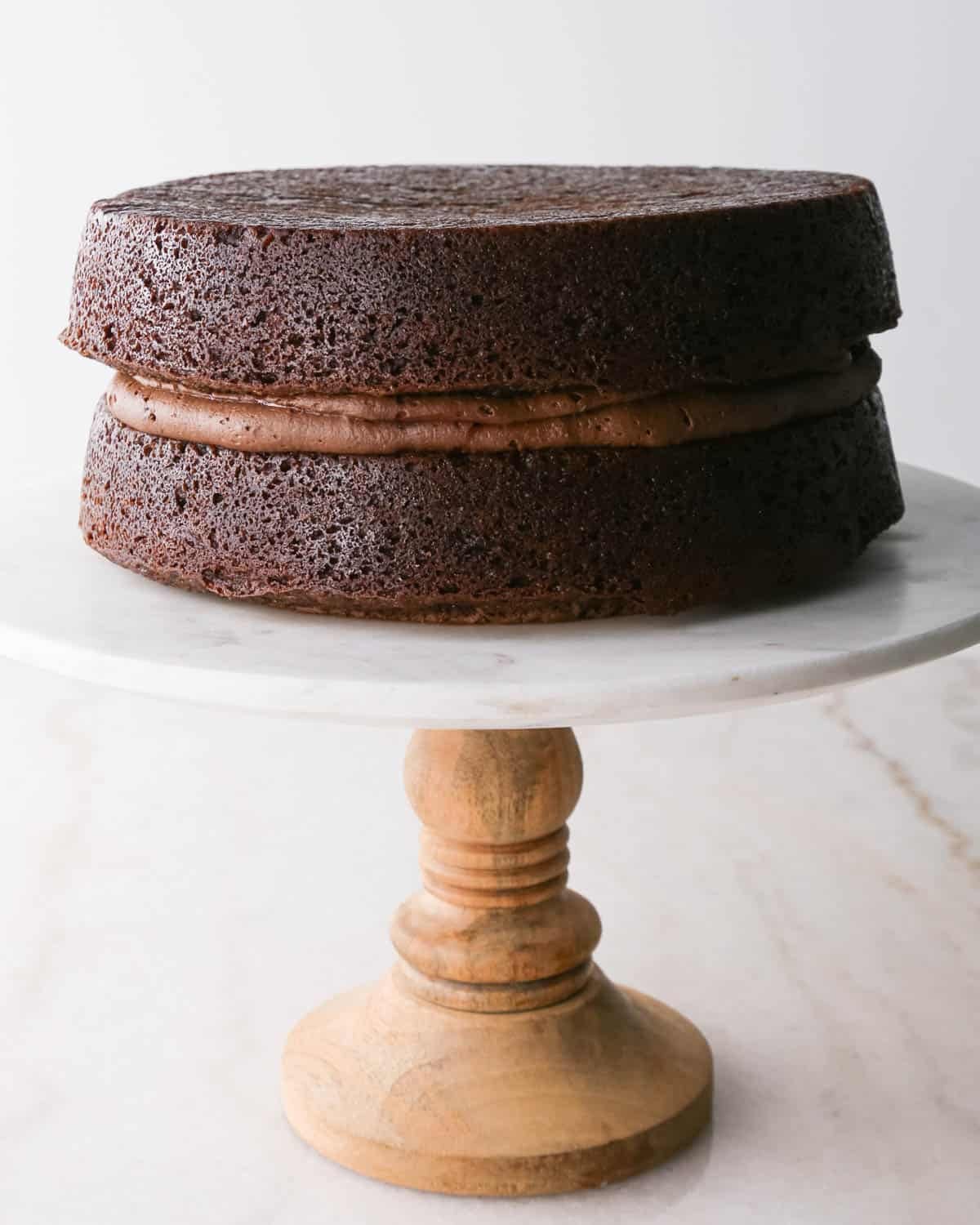 assembling chocolate raspberry cake - top cake layer put over the filling layer on a white marble cake stand with a wood base