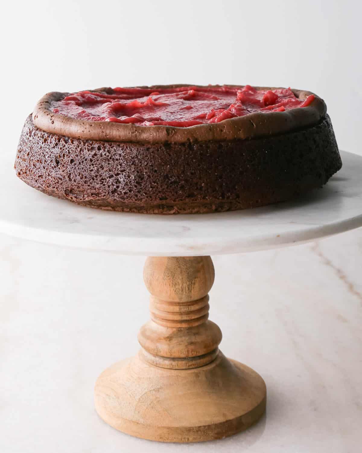 assembling chocolate raspberry cake - raspberry filling spread into a ring of chocolate frosting on the first layer of cake on a white marble cake stand with a wood base