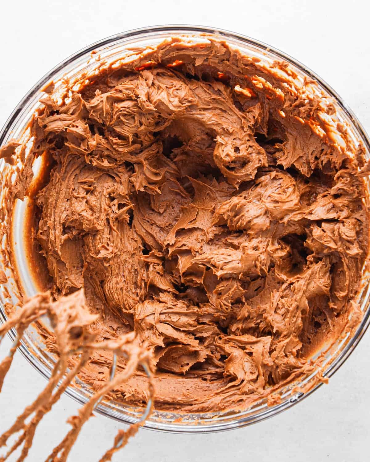 chocolate buttercream frosting in a glass bowl with two beaters on the bottom left side