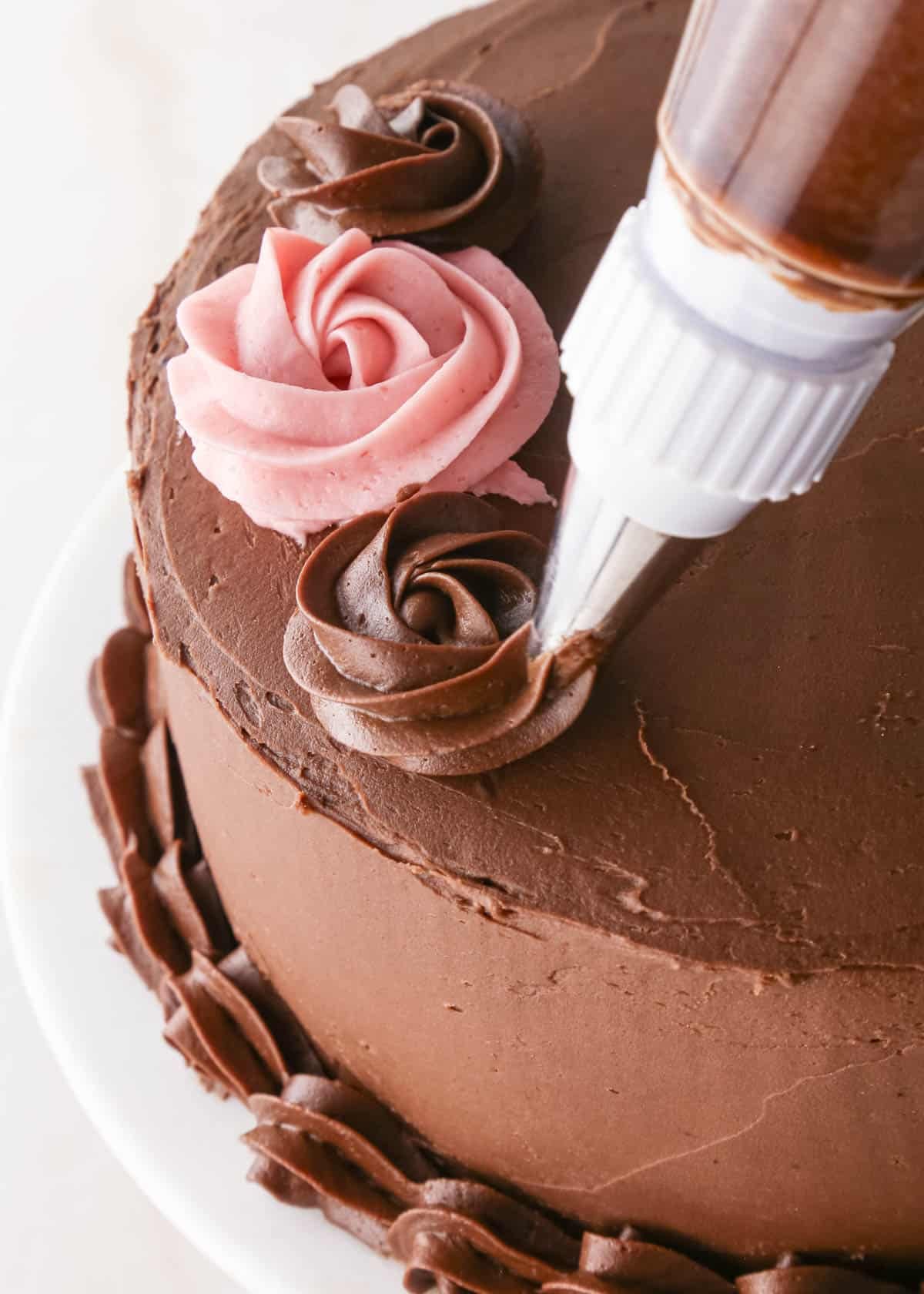 decorating a chocolate raspberry cake with a piping tip making a chocolate rose on top of the cake