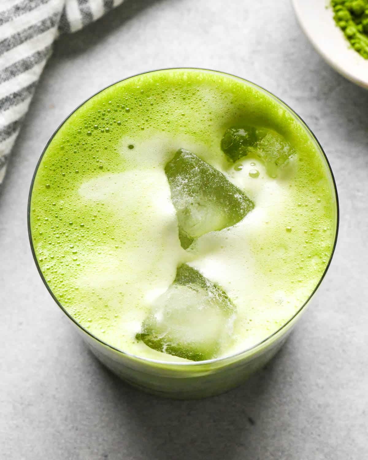 overhead photo of an iced matcha latte in a glass cup on a gray surface