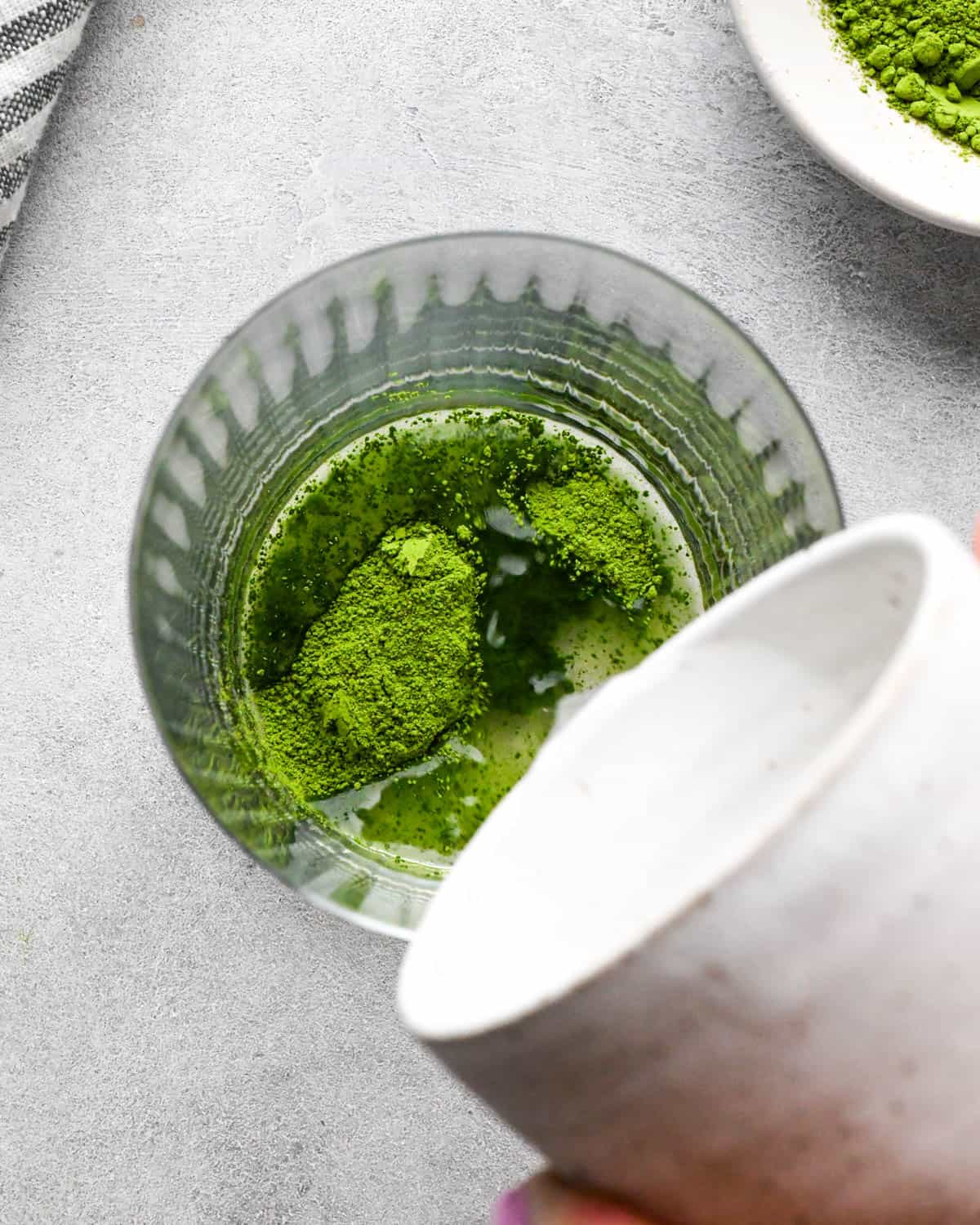 photo showing how to make an iced matcha latte - overhead view of boiling water being poured into a glass cup