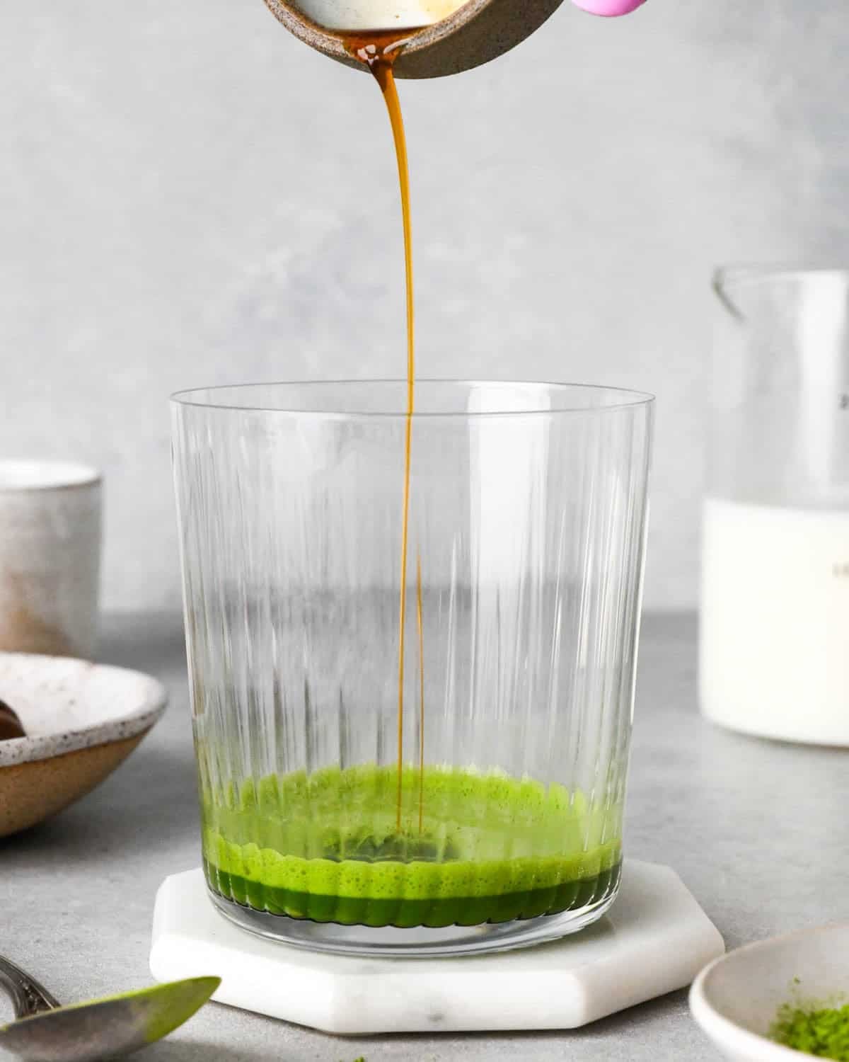 photo showing how to make an iced matcha latte - front view of vanilla being poured into a glass cup with matcha and water at the bottom