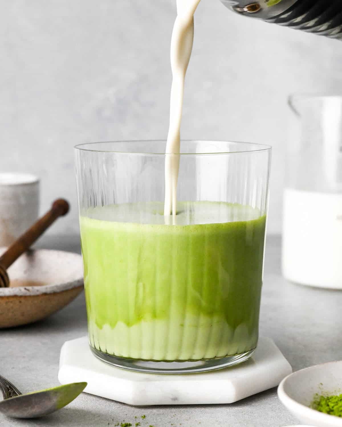 photo showing how to make an iced matcha latte - front view of frothed milk being poured into a glass cup with matcha and water at the bottom