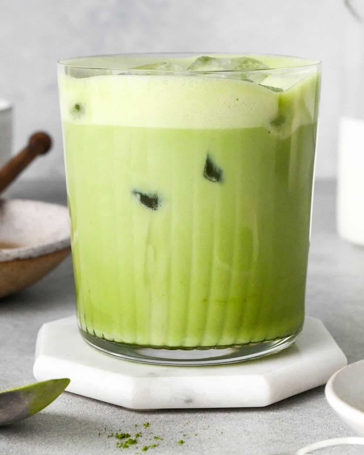front view of an iced matcha latte in a glass mug with a layer of foamy at the top