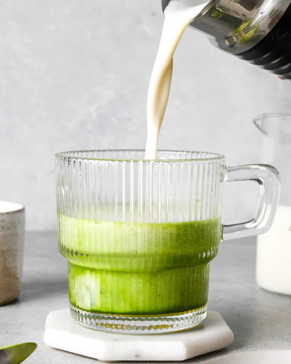 photo showing how to make a matcha latte - front view of frothed milk being poured into a glass mug with matcha powder and hot water