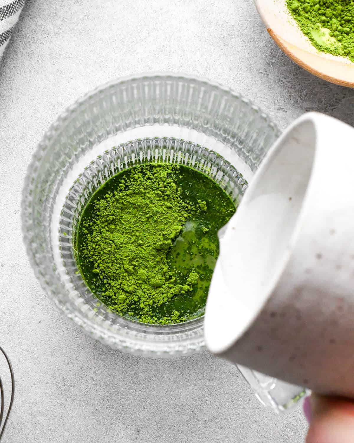 photo showing how to make a matcha latte - overhead view of hot water being poured into matcha powder in a glass mug